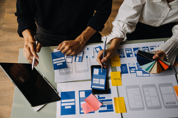 Close up ux developer and ui designer brainstorming about mobile app interface wireframe design on table with customer breif and color code at modern office.Creative digital development agency