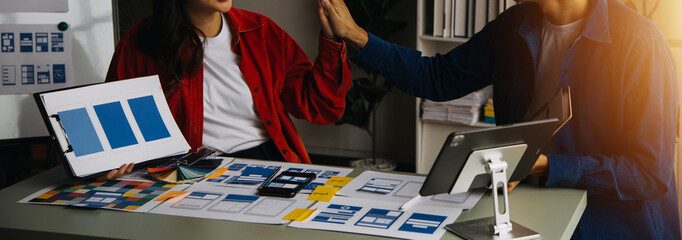 Close up ux developer and ui designer brainstorming about mobile app interface wireframe design on table with customer breif and color code at modern office.Creative digital development agency