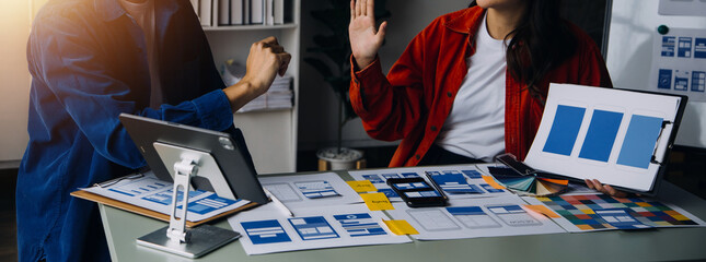 Close up ux developer and ui designer brainstorming about mobile app interface wireframe design on table with customer breif and color code at modern office.Creative digital development agency