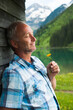 © Designpics - Portrait of mature man with eyes closed, holding flower, standing next to building at Lake Vilsalpsee, Tannheim Valley, Austria