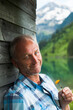 © Designpics - Portrait of mature man looking at camera, holding flower, standing next to building at Lake Vilsalpsee, Tannheim Valley, Austria