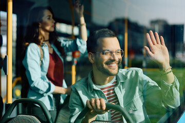 Wall Mural - Happy man waves to someone through window while riding in bus.