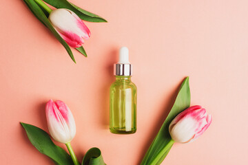 Wall Mural - Green serum bottle and tulip flowers on coral pink background. Top view, flat lay, mockup