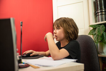 the child is sitting at the table, in front of the computer, studying the material of the online lesson.