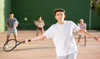 Wall Mural - Sporty young Argentinian guy playing popular team game frontenis at open-air fronton court on summer day, ready to hit rubber ball with racquet