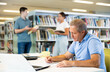 © JackF - Concentrated elderly man writing in planner while searching info in books in the library. High quality photo