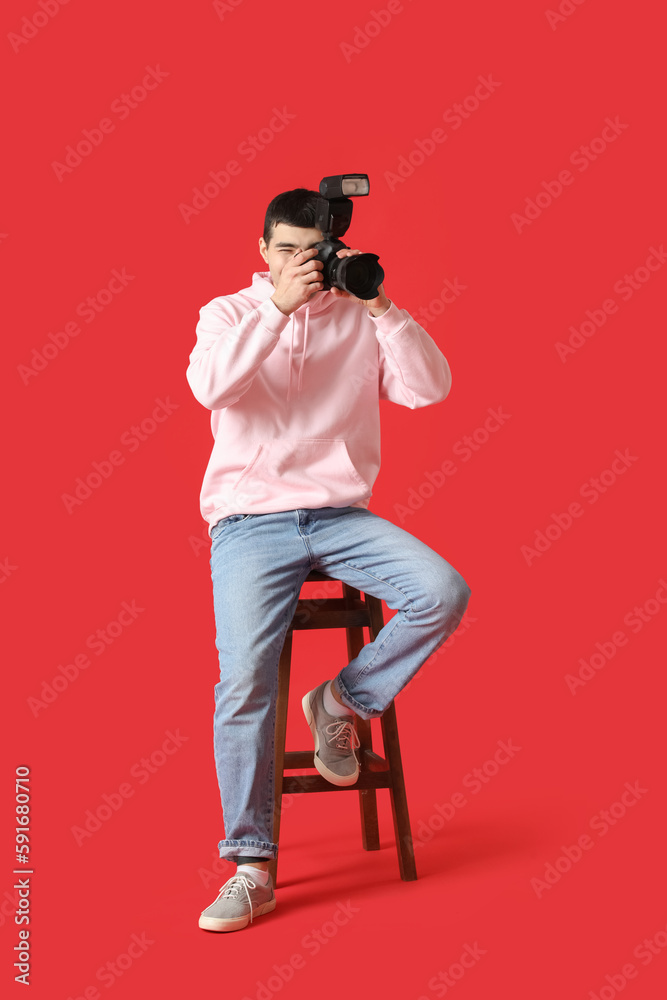 Young male photographer with professional camera sitting on red background