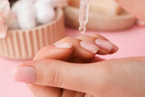 Woman applying oil onto cuticles on pink background, closeup