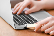 Female Hands With USB Flash Drive And Modern Laptop At Wooden Table, Closeup