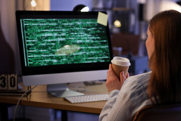 Female programmer with cup of coffee working in office at night