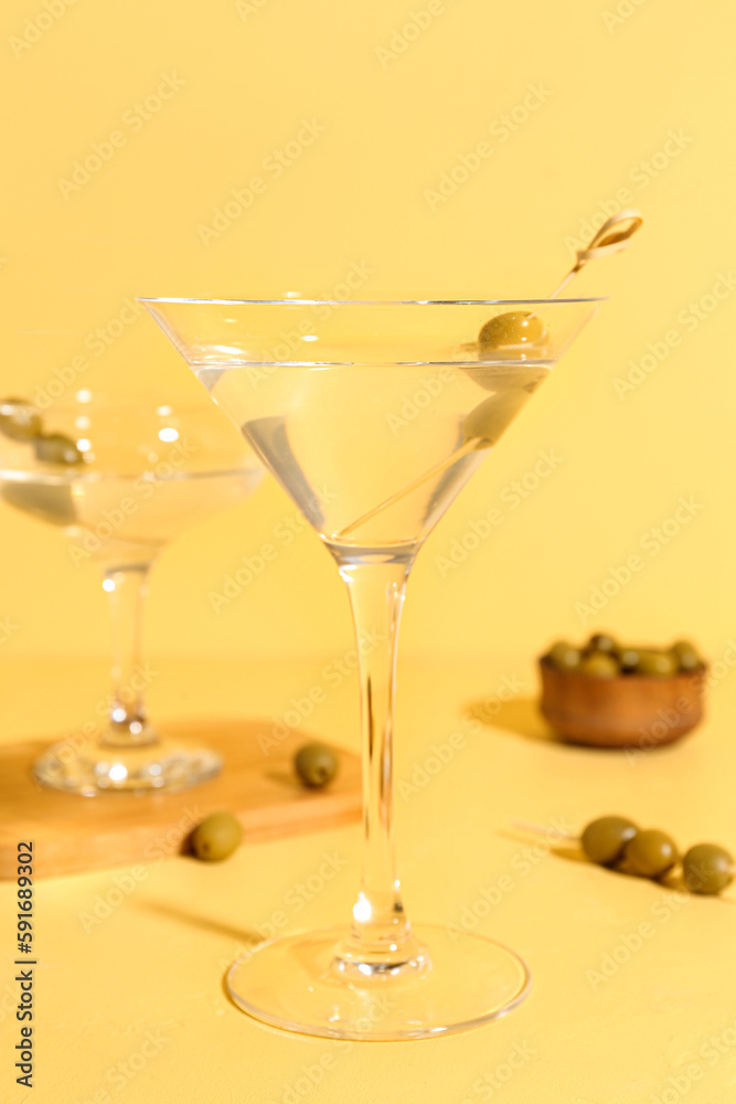 Glasses of martini with olives on yellow background