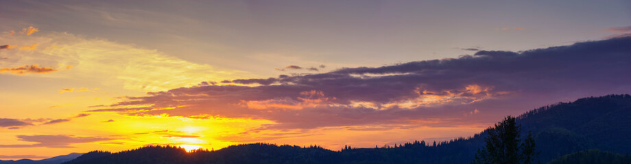 Wall Mural - sky panorama at dusk. glowing clouds above the mountain silhouette in evening light