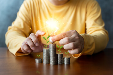 Wall Mural - Businessman holding energy-saving lamps with plants growing on coins and trees growing on coins, business start-up ideas, and financial growth.