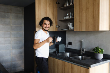 Wall Mural - latin young man preparing coffee for breakfast in kitchen at home in Mexico Latin America, hispanic people