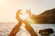 © panophotograph - Woman sea yoga. Happy woman in a white swimsuit and boho-style bracelets making a heart shape with her hands while practicing yoga on a mat by sea at sunset. Healthy lifestyle, harmony and meditation