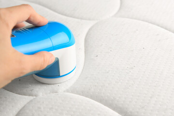 Poster - Woman using fabric shaver on mattress with lint, closeup. Space for text