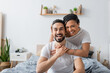 © LIGHTFIELD STUDIOS - overjoyed multiethnic couple in white t-shirts laughing at camera in bedroom at home.