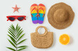 Tropical summer vacation concept with fashion bag; beach hat, flip flops and palm tree leaf  on white background. Top view from above
