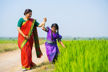 Wall Mural - Tracking shot, Girl kid playing by touching crop by holding mother hand at farmland - concept of parental caring.