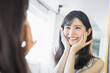 鏡の自分の顔を見て肌の状態の良さに嬉しくなり両手で頬に手を当てる30代の女性（ビューティーイメージ）