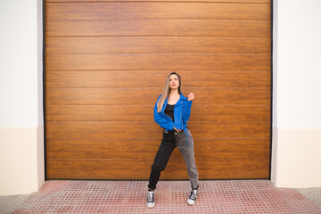 young and beautiful blonde woman dressed in black t-shirt and blue leather jacket and jeans on wooden background poses for photos doing different poses like a model. Beauty and fashion concept.