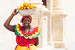Cheerful fresh fruit street vendor aka Palenquera in the Old Town of Cartagena de Indias, Colombia. Happy Afro-Colombian woman in traditional clothing, Colombian culture and lifestyle. 