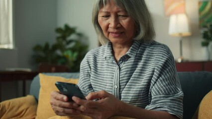 Wall Mural - Beautiful elderly woman smile using mobile phone enjoy playing social media checking email. Happy attractive grandma hand holding smartphone scrolling looking at screen sit on sofa in living room