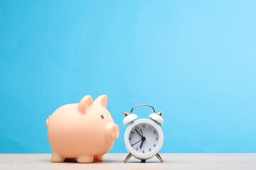 Wall Mural - Alarm clock with piggy bank on the table, blue background