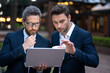 © Volodymyr - Business men team using laptop outdoor. Businessmen looking laptop with their business success in city background. Two business teams success.
