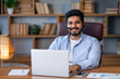 © Ivan - Portrait of smiling millennial Arabic man sit at desk in office have video call with customer or client, happy young Arabian male employee talk on webcam, speak on online webinar