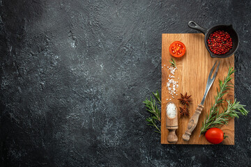 Wall Mural - Chopping board, seasonings and rosemary on dark background. cooking background. place for text, top view