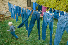 Young Boy Runs Through Jeans That Hang On A Clothes Line; Lincoln, Nebraska, United States Of America