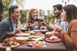 © Lomb - Friends Enjoying Outdoor Dinner - A group of friends aged 25-45 enjoying skewers and wine in the garden. A bearded man and a mature blonde woman toast during a pleasant summer evening.