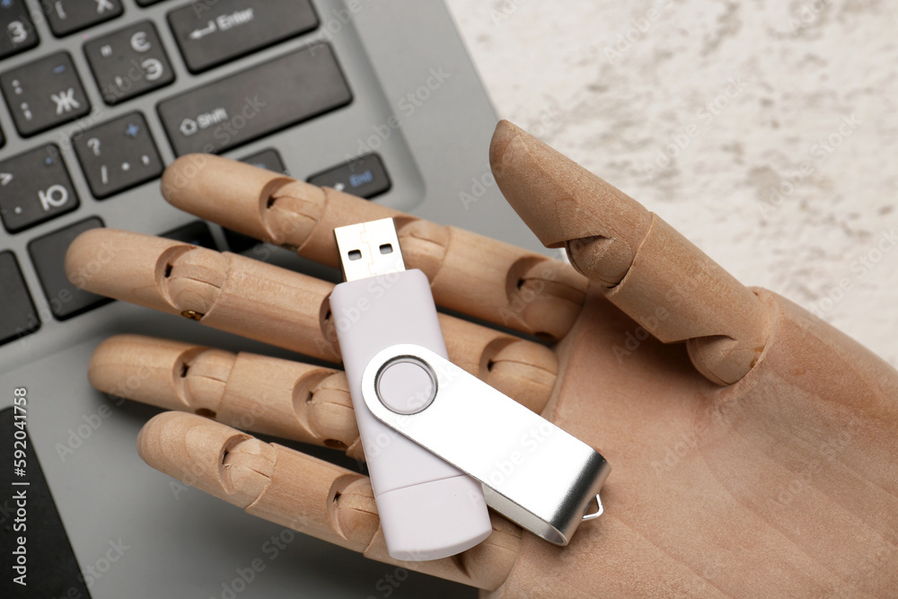 Wooden hand with USB flash drive and laptop on light background, closeup