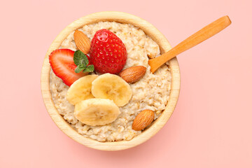 Bowl with tasty oatmeal, almonds, bananas and strawberries on pink background