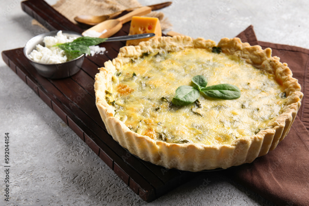 Board with delicious quiche, spinach leaves and cheese on grey grunge background
