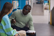 © Seventyfour - Portrait of black young man as mental health therapist talking to teenage girl in college library, copy space