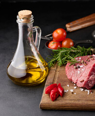 Wall Mural - Raw piece of beef with spices pepper, rosemary sprig, salt and olive oil on a wooden board, black background