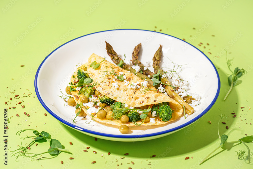 Tasty omelet with broccoli, pea and asparagus on green background