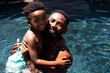 Portrait of cheerful african american shirtless father carrying son while swimming in pool at resort