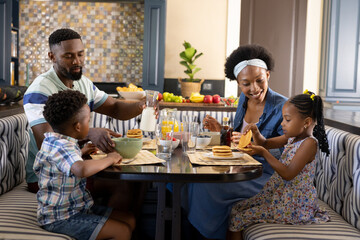 Happy african american parents and children having breakfast at dining table in morning, copy space