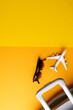 Airplane model, sunglasses and suitcase on yellow background with copy space