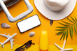 Smartphone with copy space, airplane model, suitcase, sunscreen, straw hat on yellow background