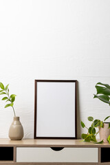 Vertical of black empty frame with copy space and plants in pots on table against white wall