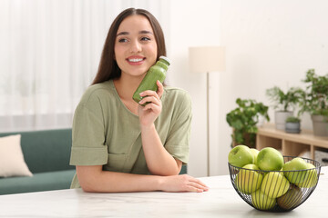 Poster - Beautiful woman with bottle of delicious smoothie at table indoors