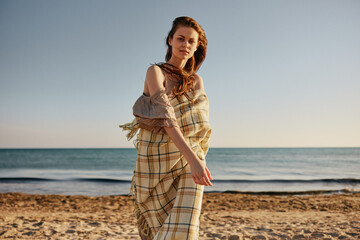 Wall Mural - red-haired woman walks along the sea coast wrapped in a blanket