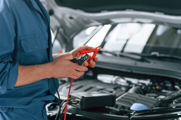 Testing breakage by using electrical terminals. Man in blue uniform is working in the car service