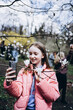 © Анна Молько - girl in the park take selfie on phone with magnolia flowers. video call in park