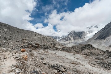 Rocky terrain against snowy mountains covered with clouds and a blue sky