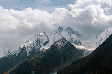 Wall Mural - View of snow-covered mountain peaks in the clouds on a sunny autumn day